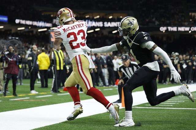 A San Francisco 49ers player with the ball runs near the sideline while a New Orleans Saints player reaches out trying to stop him.